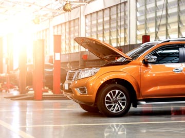 Ein orangefarbenes SUV steht in einer gut beleuchteten Auto-Werkstatt bei Autoankauf Lübeck, dessen Motorhaube offen ist und den Motor zeigt.